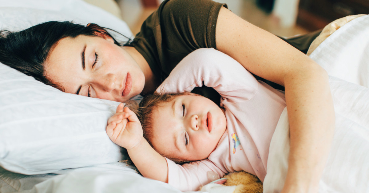 Mother asleep while embracing her baby child