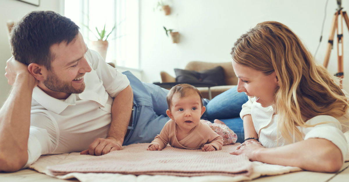 a father and mother playing with their infant child on the floor