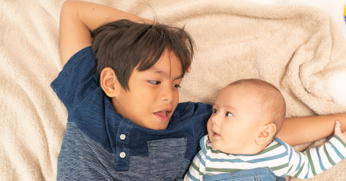 older brother laying beside younger infant sibling.