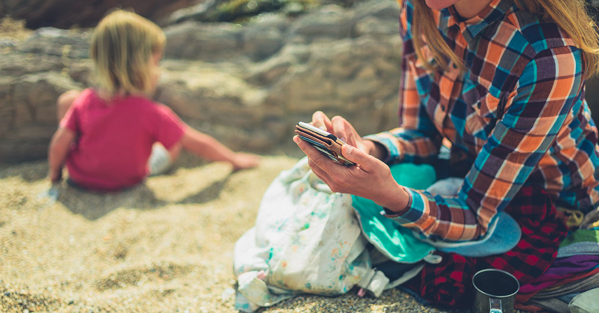 parent using smartphone with child seemingly ignored in background