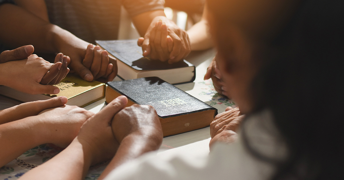 hands held together in a circle praying around a bible