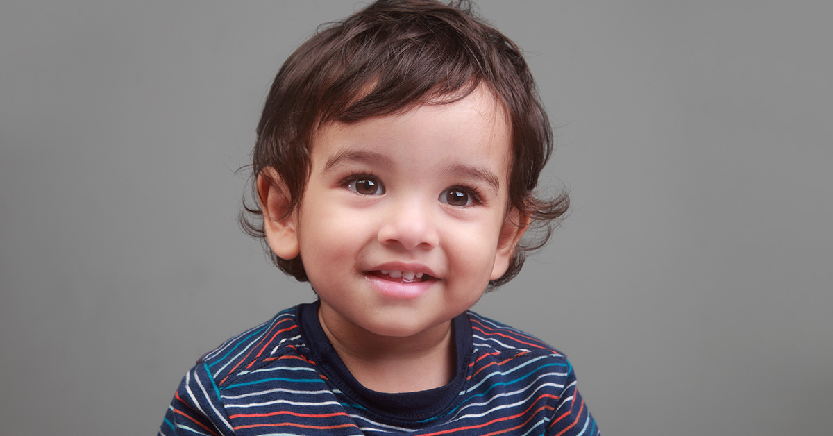 young boy with dark hair and eyes wearing a blue, grey, and red striped shirt