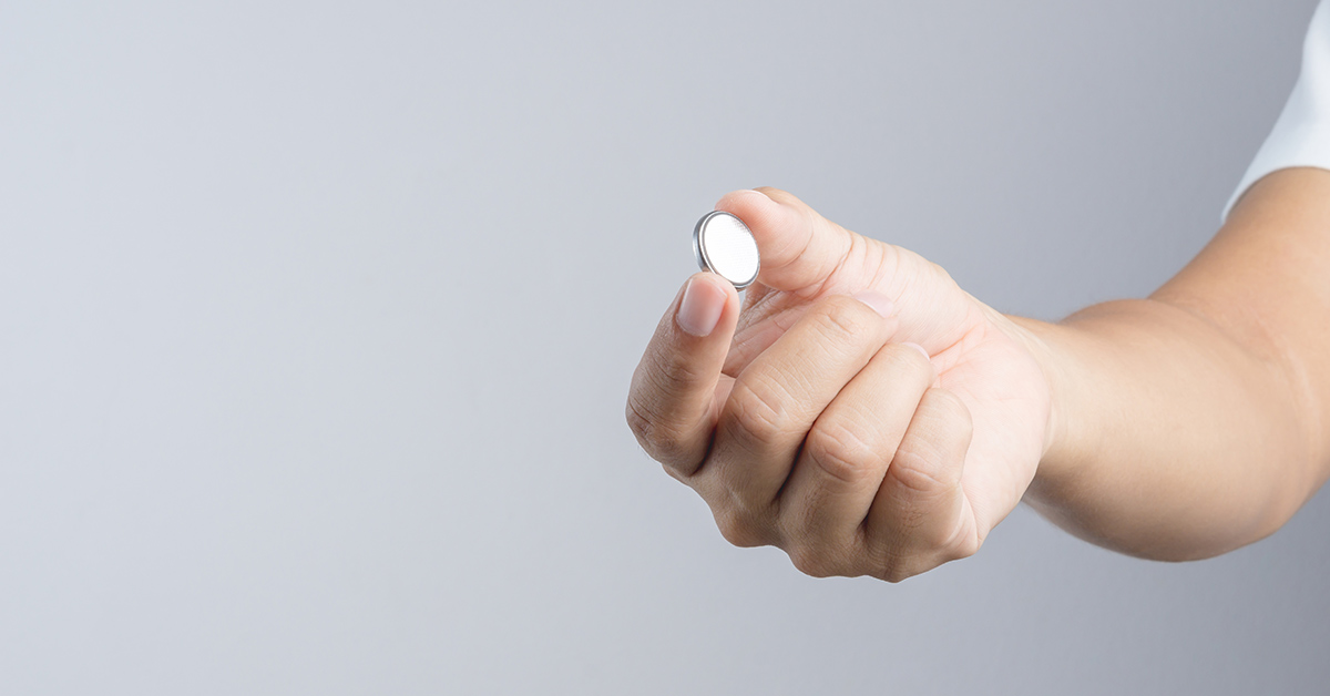 button battery being held in a hand between the index finger and thu,b