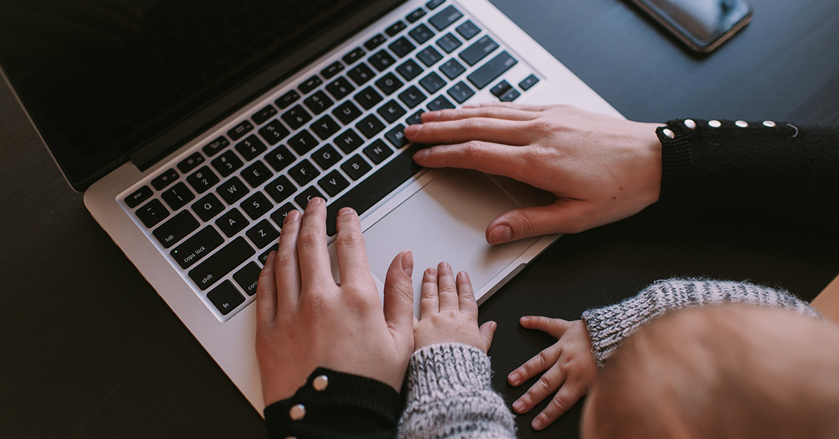 parent and infant typing on laptop keyboard