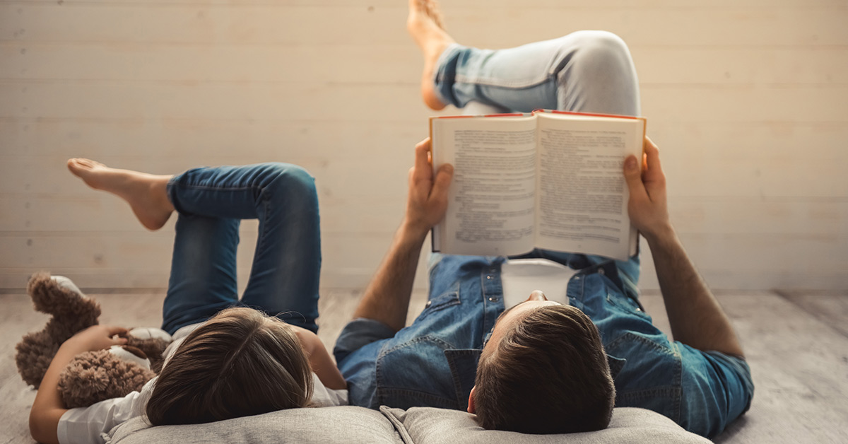father and daughter laying down. Father is reading to his daughter