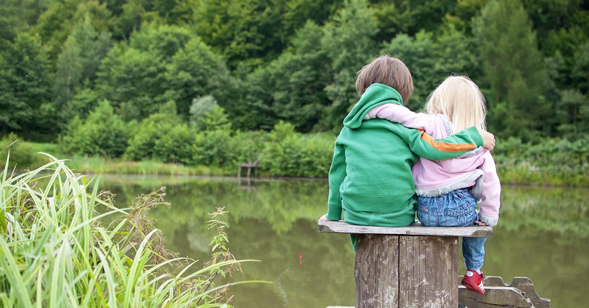 brother and sister sitting by a small lake on an tree stump