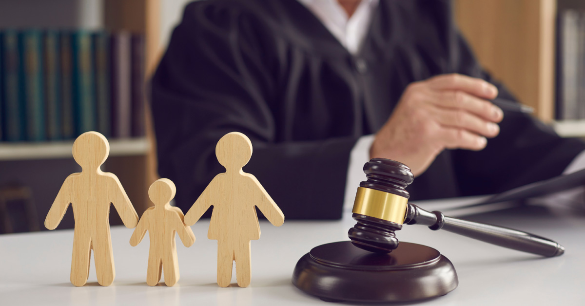 a judge at the stand with a judge hammer and wooden figures depicting a family (father, child, and mother) in the foreground