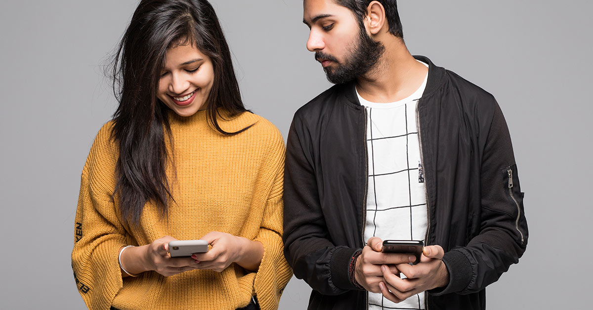 man looking over woman's shoulder to look at her phone while she uses it