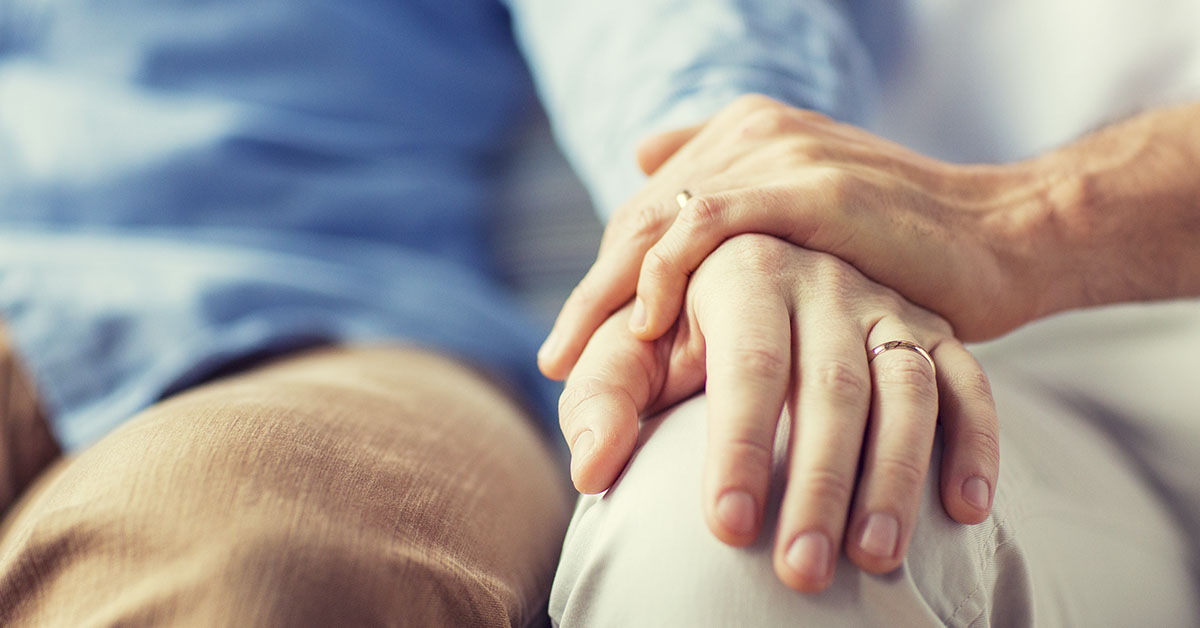 one hand on a knee with a hand ontop of that. both male hands with wedding rings