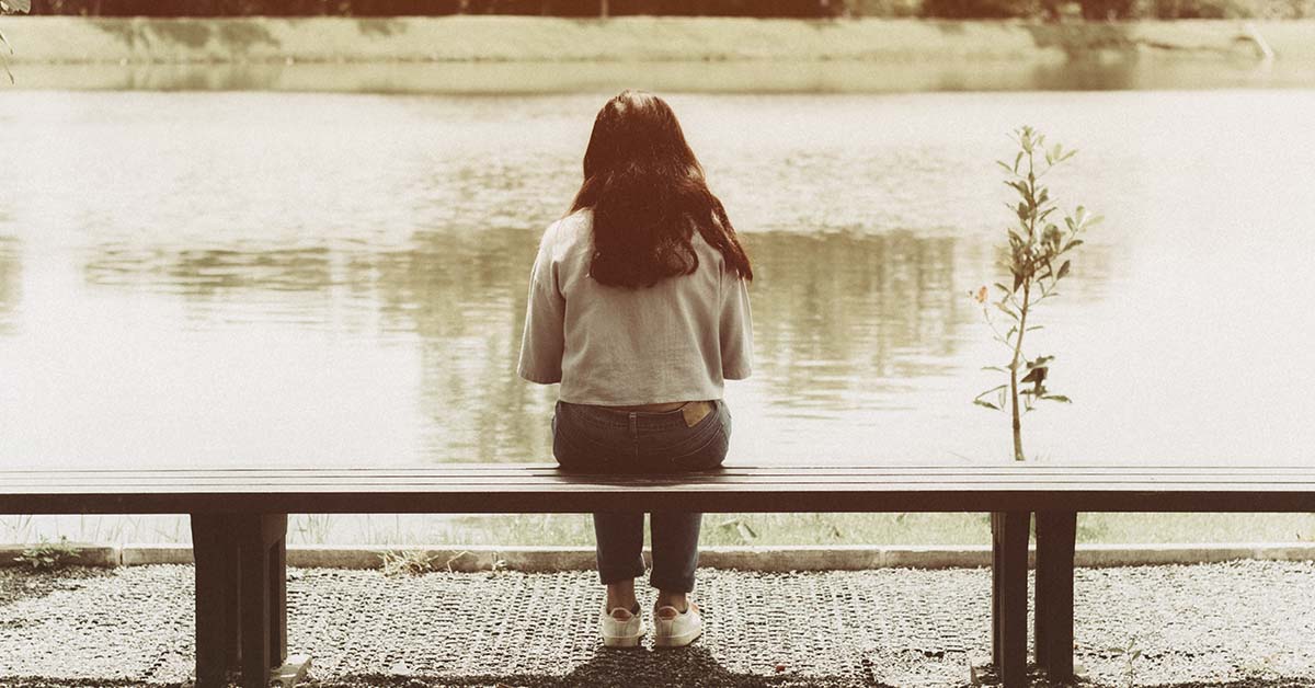 woman sitting on a bench by body of water