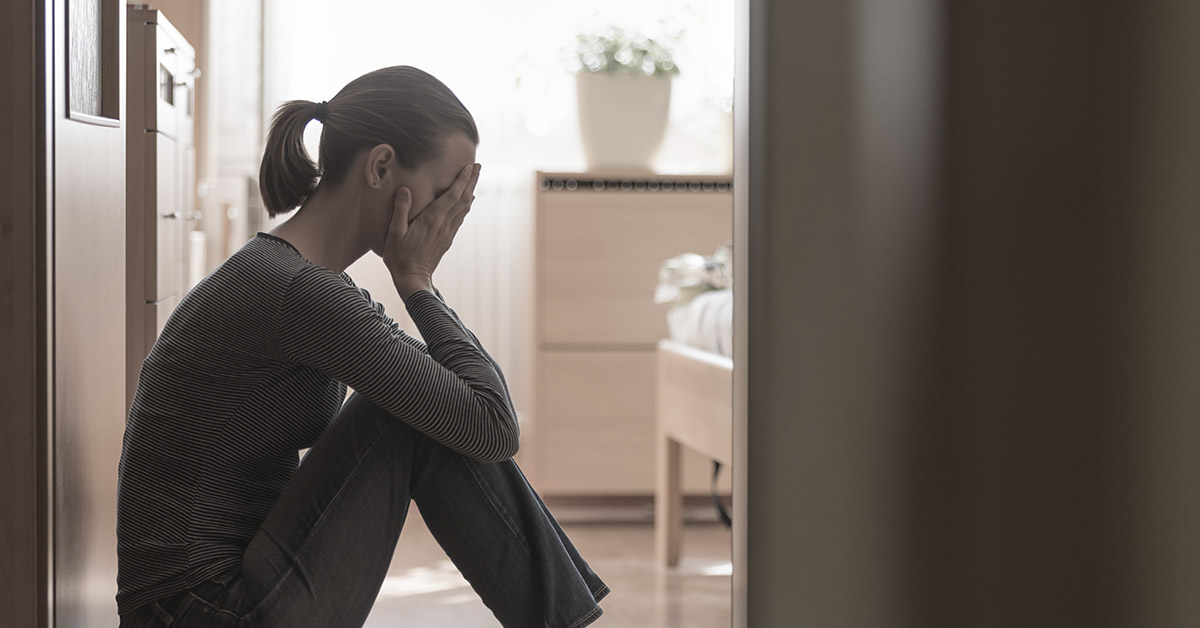 distraught woman sitting down against wall with face in her palms