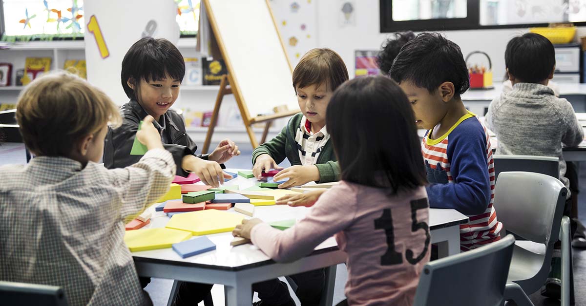 children in classroom setting sitting around a table during arts and crafts