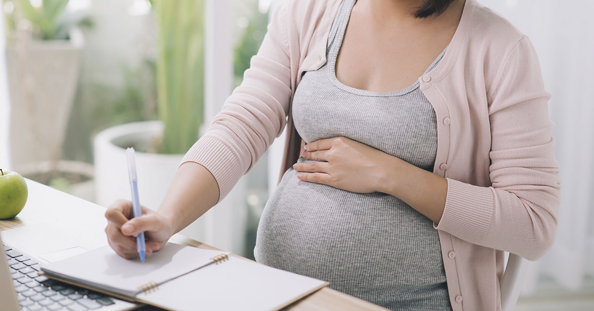 pregnant woman sitting at desk writing