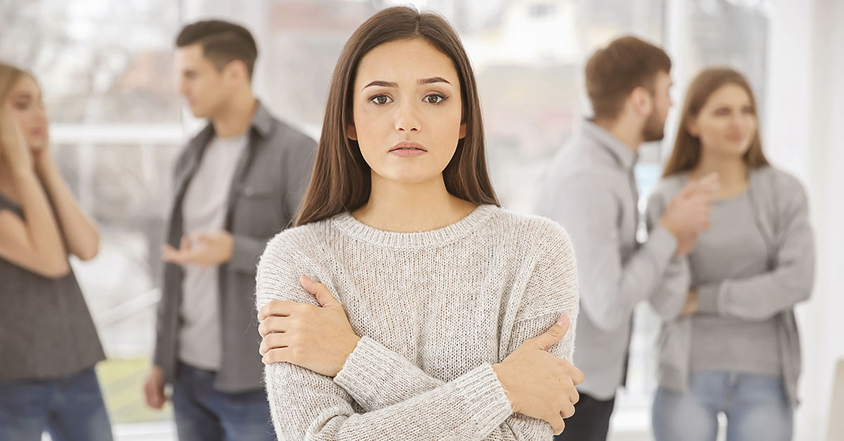 Anti social concept. Woman at a social gathering by herself with arms crossed. People can be seen socializing in background.