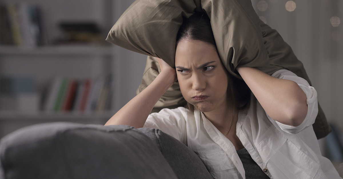 woman with pillow placed over head and ears in frustration