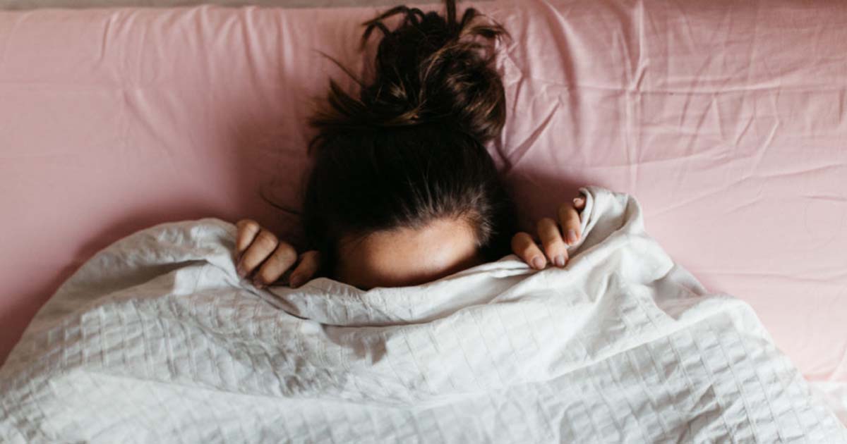 woman in bed with pink sheets under her white blanket