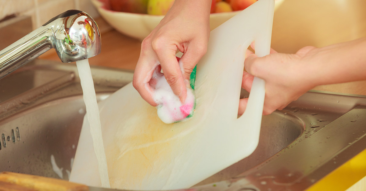 person cleaning a plastic cutting board in their kitchen sink