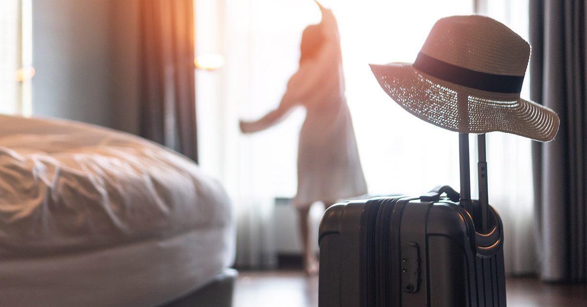 person just arriving in their hotel room. Luggage in foreground, woman looking out window in background