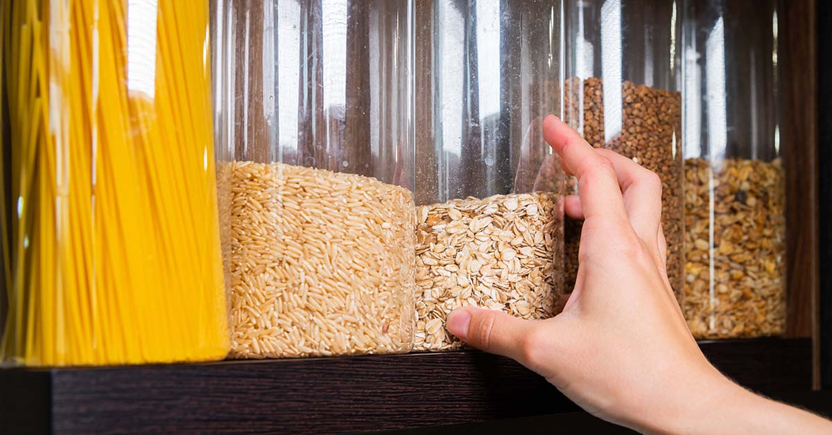 Hand reaching for glass jars filled with various grains in a pantry