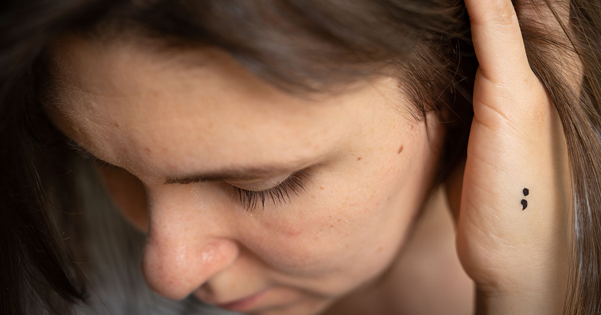 person with semicolon tattoo on hand
