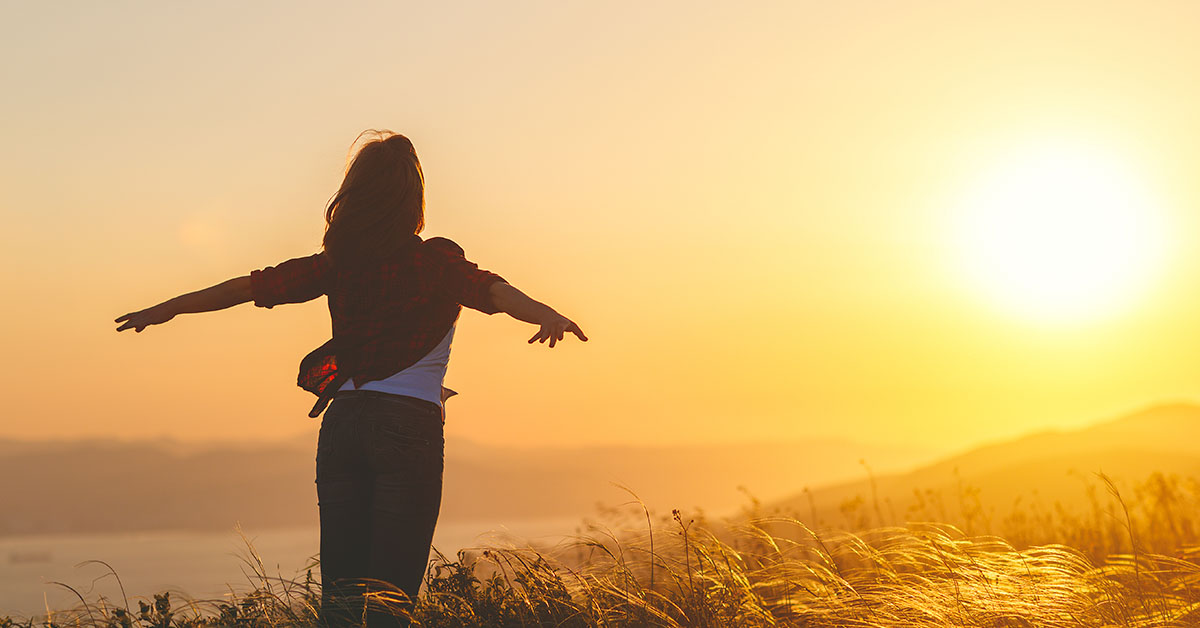 Happy woman on the sunset in nature in summer with open hands