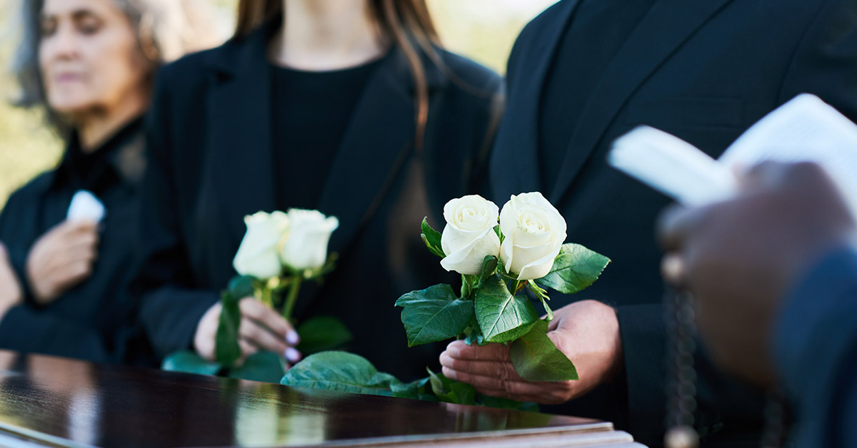 people holding white roses at funeral