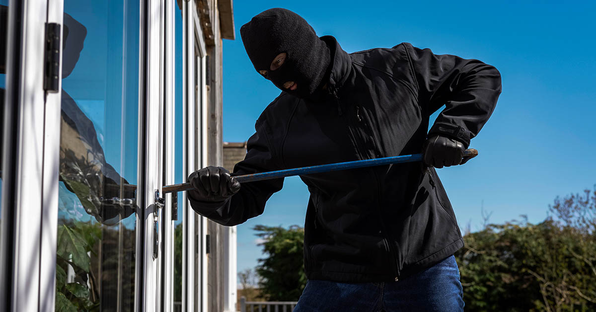 burglar wearing all black with balaclava breaking into a home using a crow bar. Break-in, breaking and entering concept