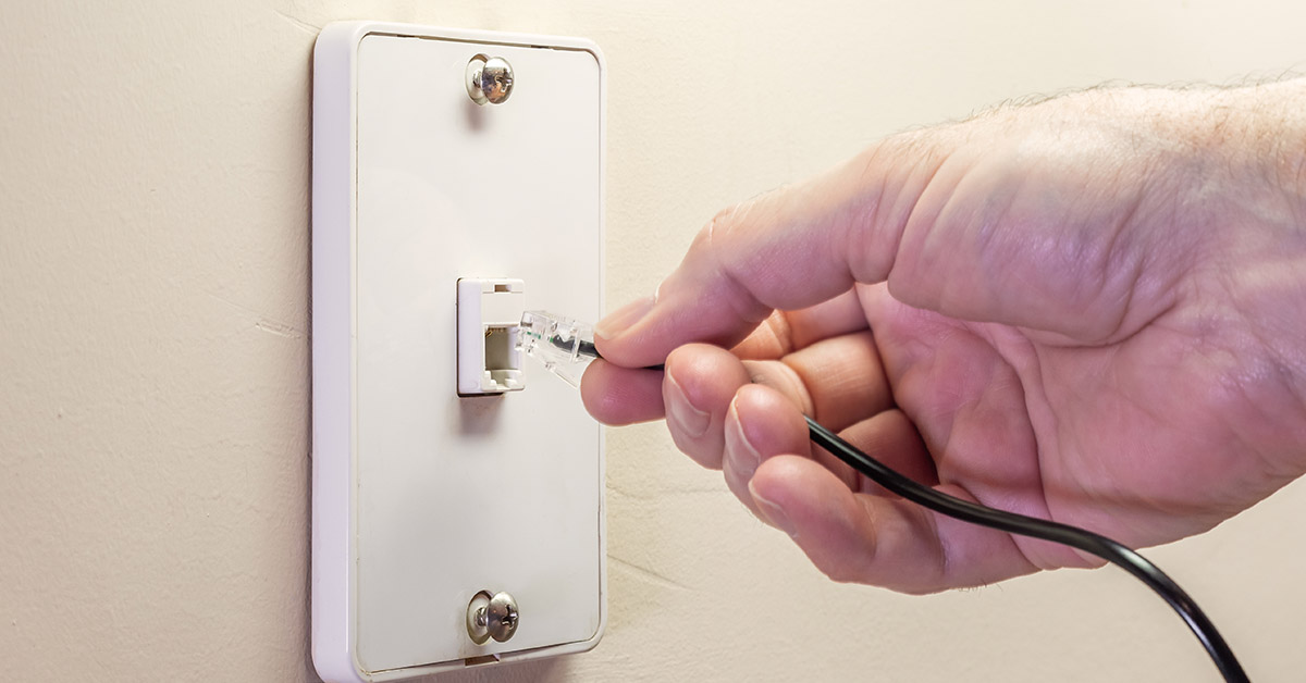 person plugging phone cable into phone jack