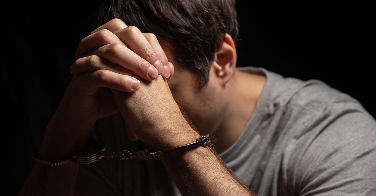 Man, criminal and handcuffs for interrogation, crime or money laundering in arrest on table in room. Closeup of male person, gangster or suspect in jail, justice or guilty for fraud, theft or scam