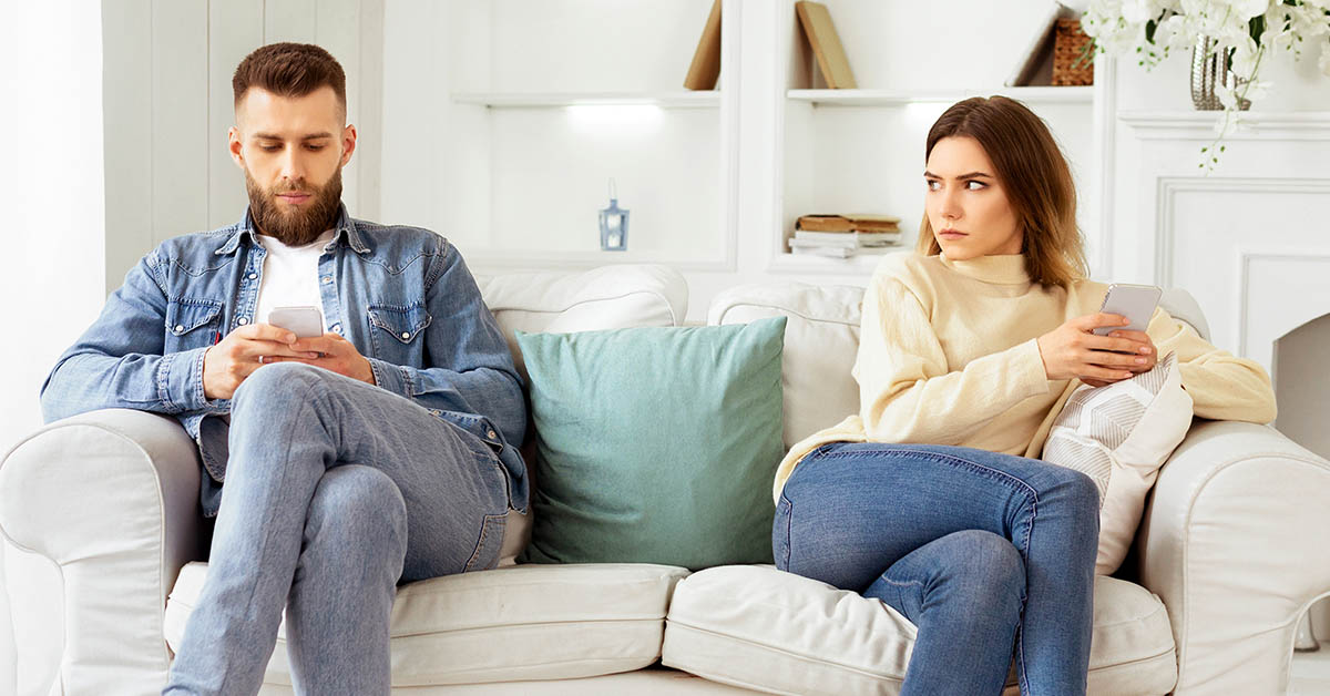 Stubborn couple sit on couch back to back avoid talking after fight, offended man and woman separated on sofa ignoring one another, husband and wife not looking in eyes. Family conflict concept