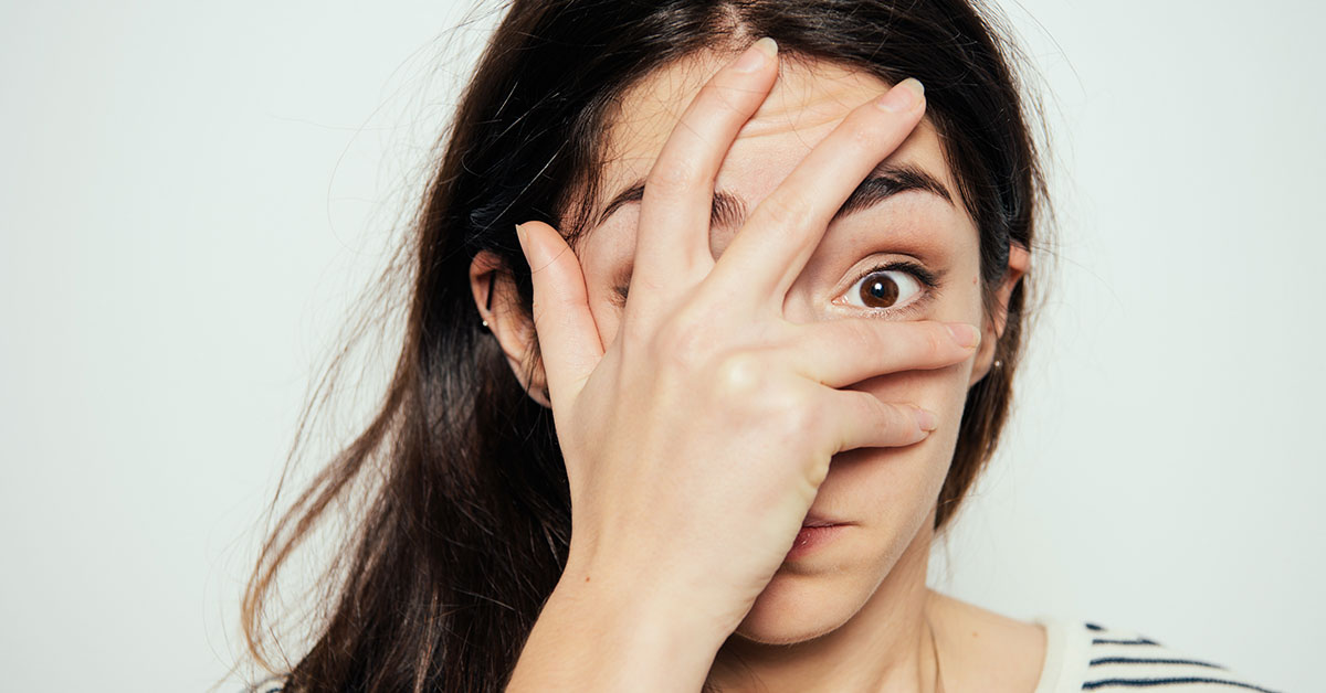 surprised woman with hand placed on face while looking between her fingers