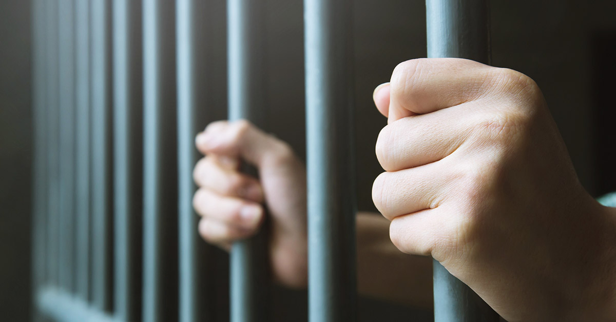 hands holding on to bars on door or jail cell