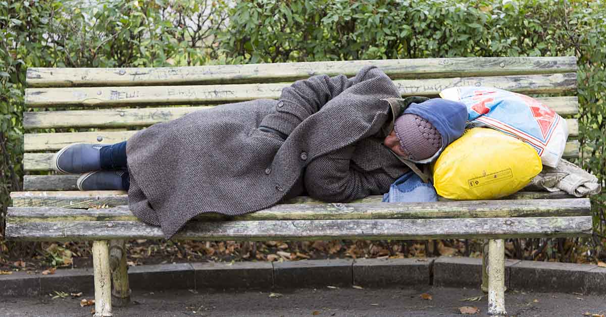 person experiencing homelessness sleeping rough on a park bench
