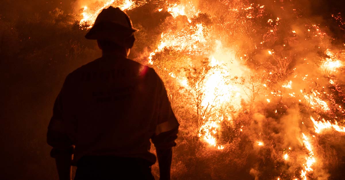 firefighter with large blazing fire in background