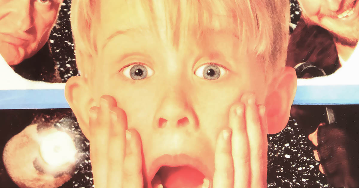 Cover for Home Alone movie featuring Kevin McCallister and the two Burglars peering through window behind him.