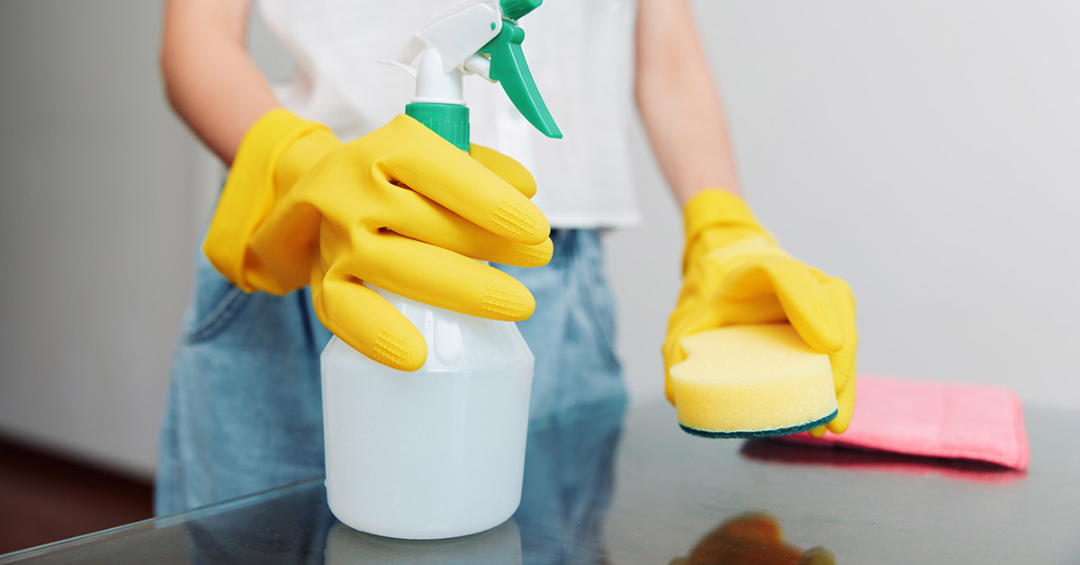 woman wearing yellow latex gloves holding a spray bottle and a sponge. Spring cleaning concept