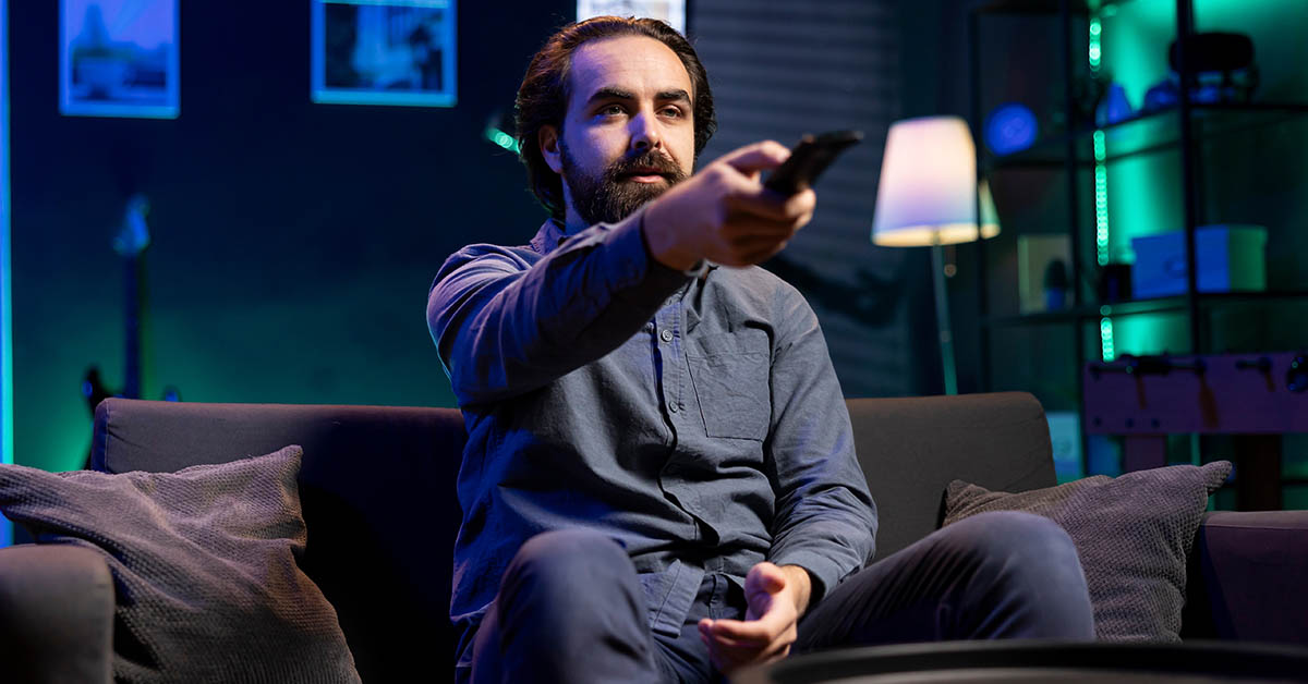 man sitting on couch pointing TV remote