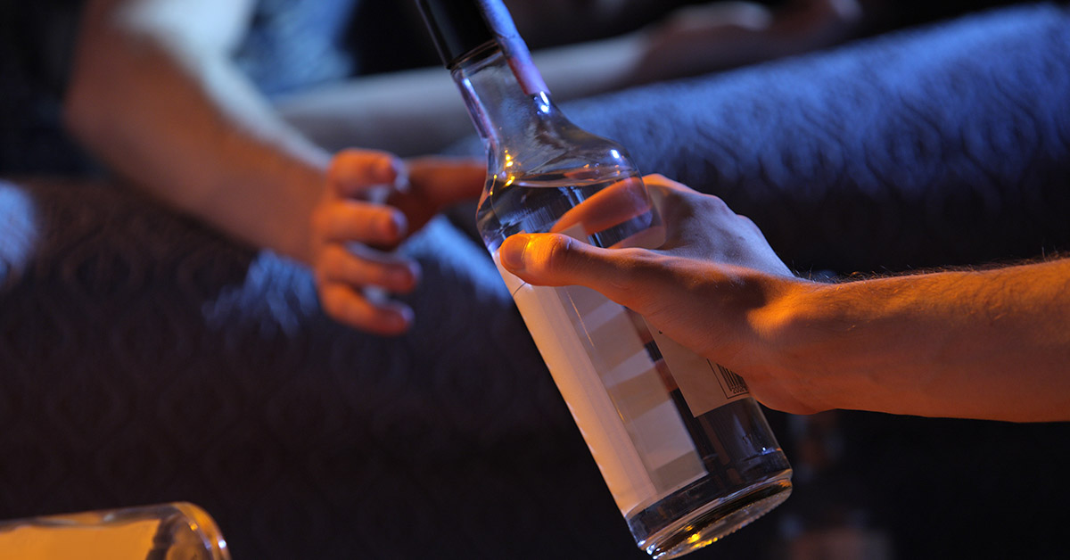 young people handing a bottle of hard liquor to someone else. teenage alcohol consumption concept