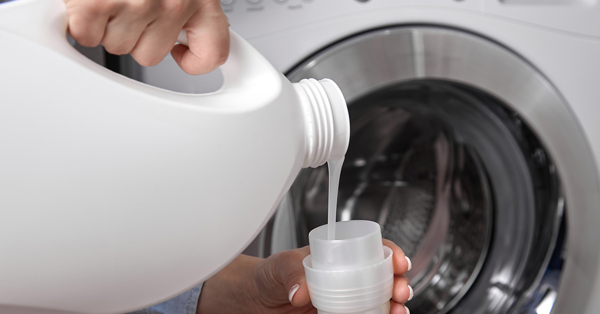 pouring detergent into measuring cup to be dispensed into front load washer
