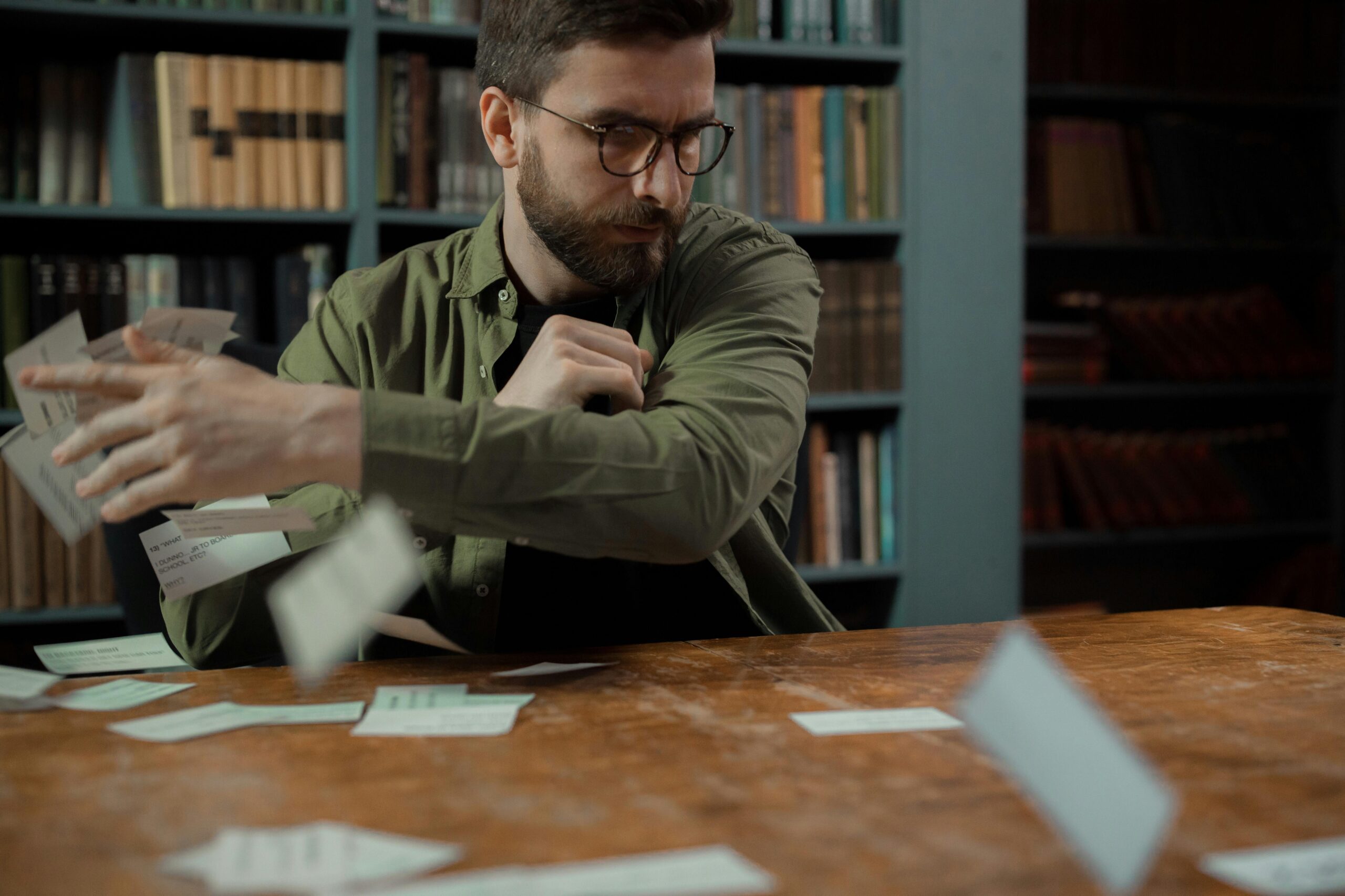 Man in Glasses Throwing Cards on Desk in Library