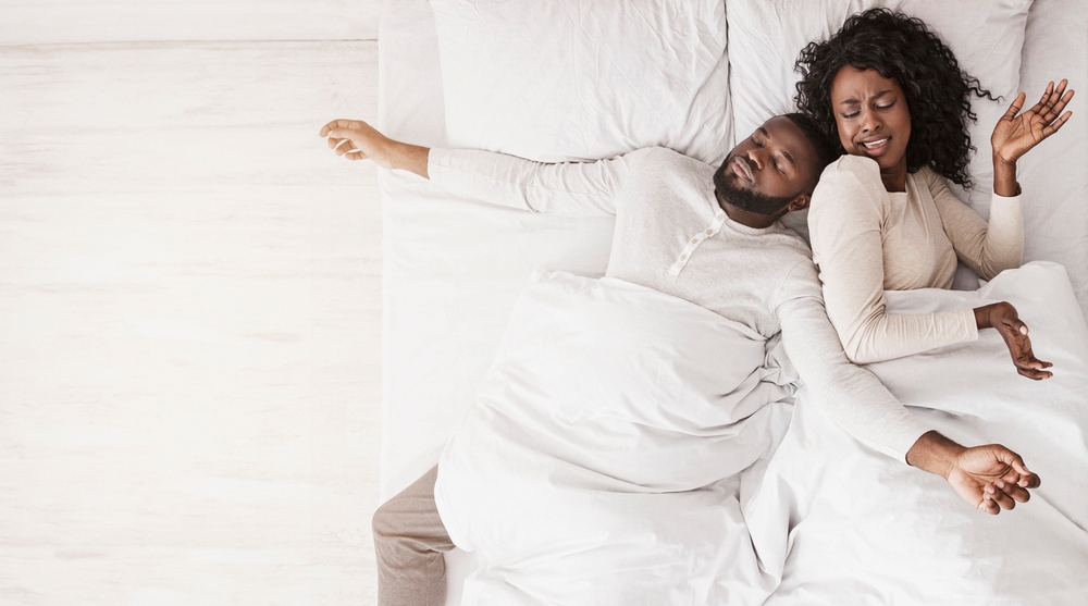No space for two. Annoyed black wife angry to husband that sprawled out all over bed, lying down with arms and legs stretched out wide, top view