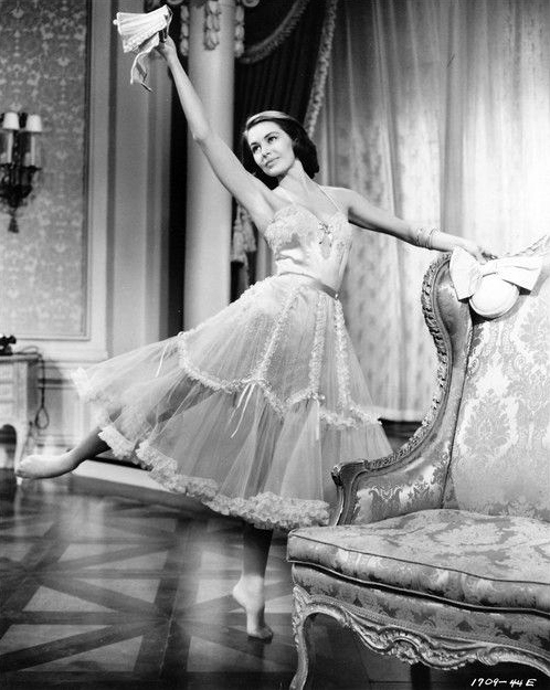 Cyd Charisse dancing next to an ornate chair in a Helen Rose ball gown for Silk Stockings, 1957.