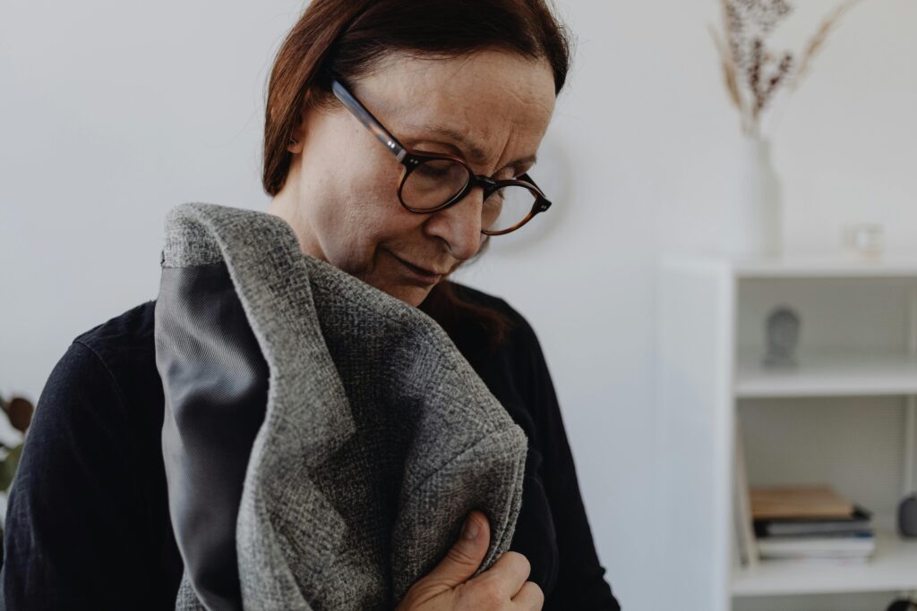 A woman gently holding and smelling a piece of clothing, lost in thought and memory.