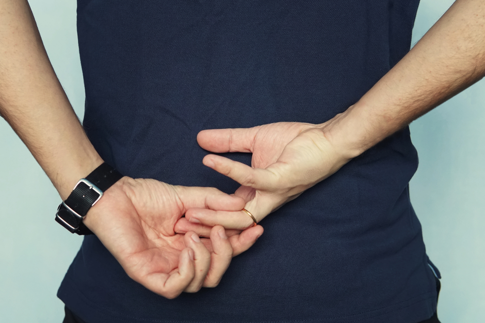 a man in struggling to remove wedding ring from his finger holding hands behind his back. concept of treason. Husband cheats on wife. cheating wife