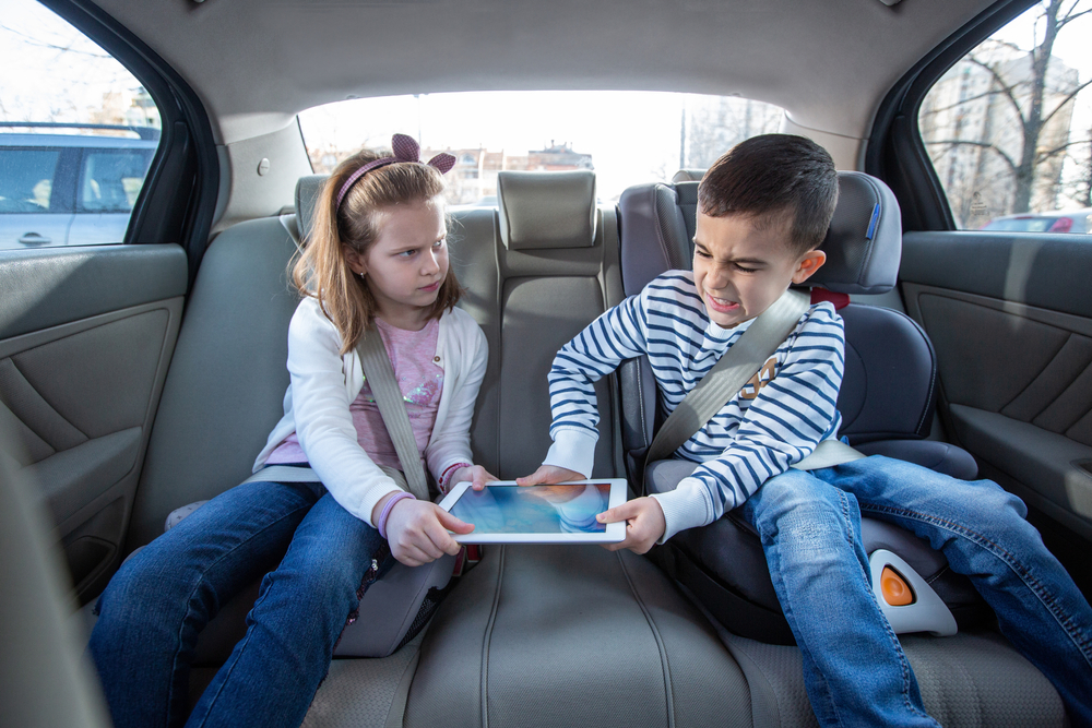 Brother and sister fighting over digital tablet on the back seat of the car, kids concept